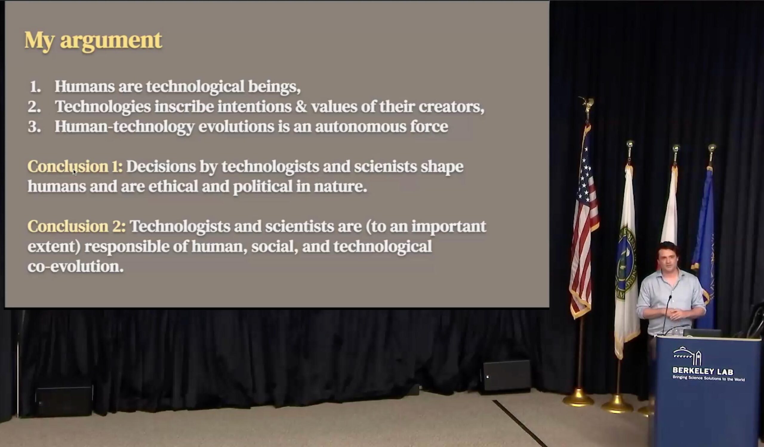 Ben Zevenbergen at the podium showing a slide entitled "My argument" that shows a bulleted list with "1. Humans are technological beings, 2. Technologies inscribe intentions & values of their creators, 3. Human-technology evolutions s an autonomous force," and then "Conclusion 1: Decisions by technologists and scientists shape humans and are ethical and political in nature" and "Conclusion 2: Technologists and scientists are (to an important extent) responsible of human, social, and technological co-evolution."