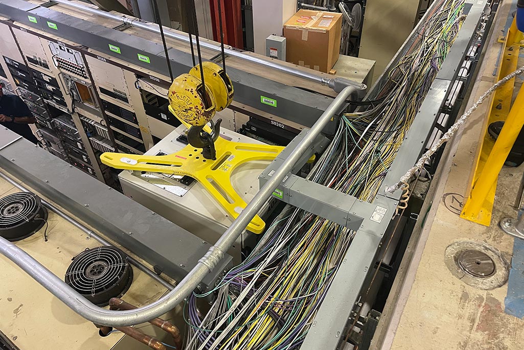 An up-close view of the new rack lift fixture (the yellow X-shaped device) affixed to the top of a rack during a crane move in the ALS. Credit: Kyle McCombs, Berkeley Lab