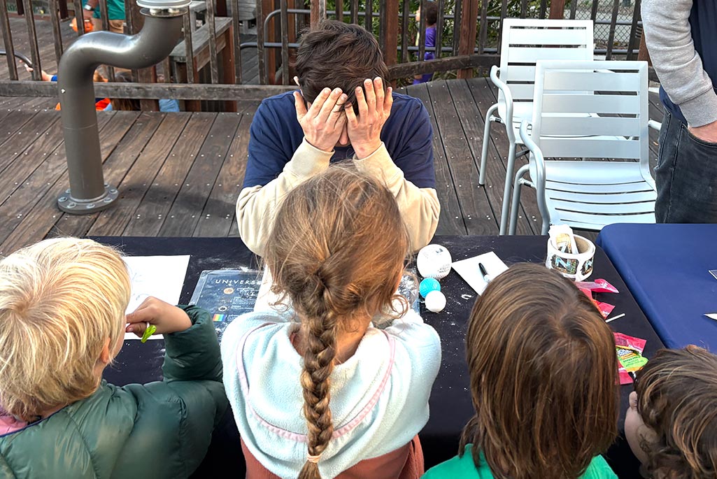 Ibles Olcina instructs young event participants to cover their eyes to set up a demonstration about how scientists use detectors to search for dark matter. Credit: Emily Perry, Berkeley Lab