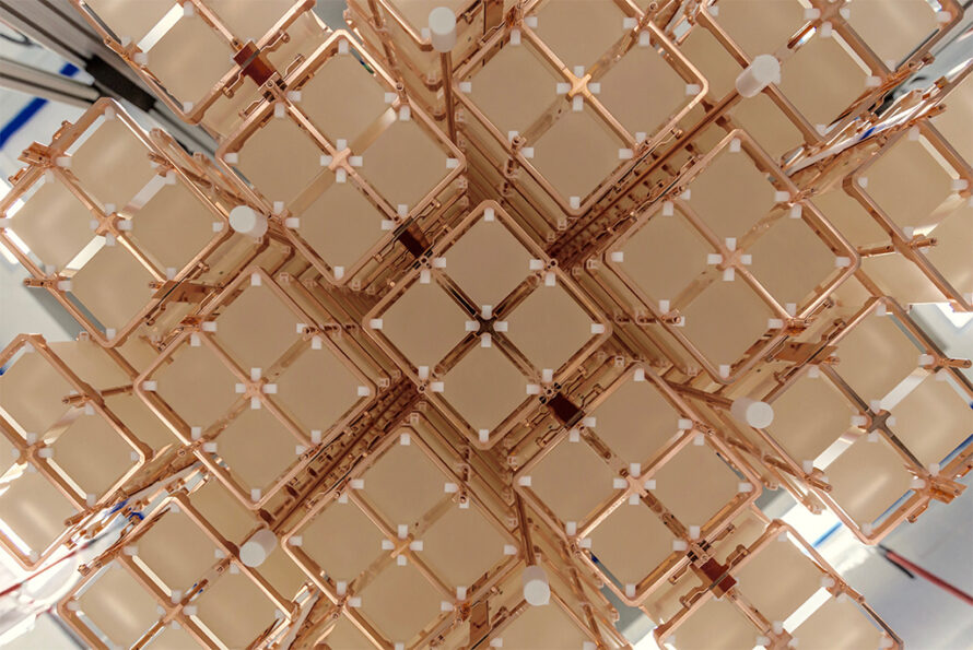 The CUORE detector has 19 copper-framed “towers” that each house a matrix of 52 cube-shaped crystals. Credit: Yury Suvorov/CUORE collaboration. Alt text: Close-up view of an array of cubic, pale crystals held in a copper framework. The structure is composed of multiple repeating units arranged in a symmetrical, grid-like pattern, with small white spacers at the intersections.
