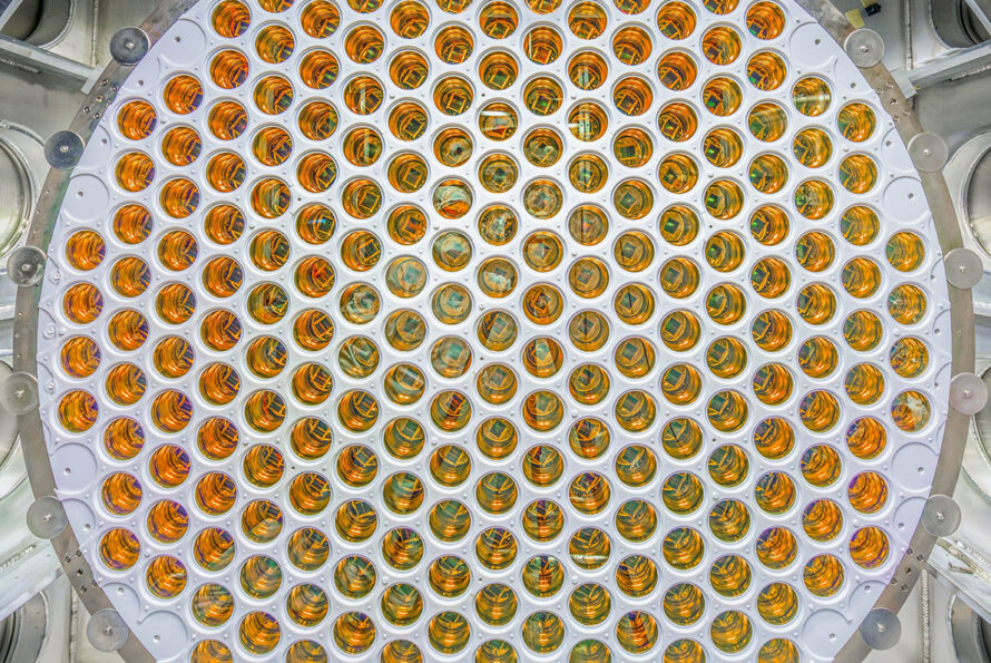 Caption: Photomultiplier tubes inside the LZ detector are designed to capture faint flashes of UV light that could signal a dark matter interaction. Credit: Matthew Kapust/Sanford Underground Research Facility Alt text: A circular array of amber, glossy photomultiplier tubes arranged in a grid pattern.