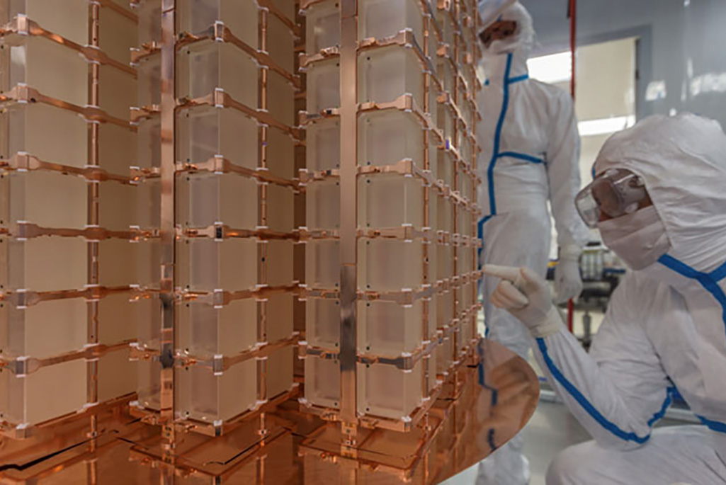research scientist examines a crystal of the CUORE detector, an array of 19 towers containing nearly 1000 cryogenic calorimeters. The copper support structures provide strong thermal coupling to the CUORE cryostat (not shown), which maintains the detector close to absolute zero (0.010 K). (Credit: CUORE Collaboration)