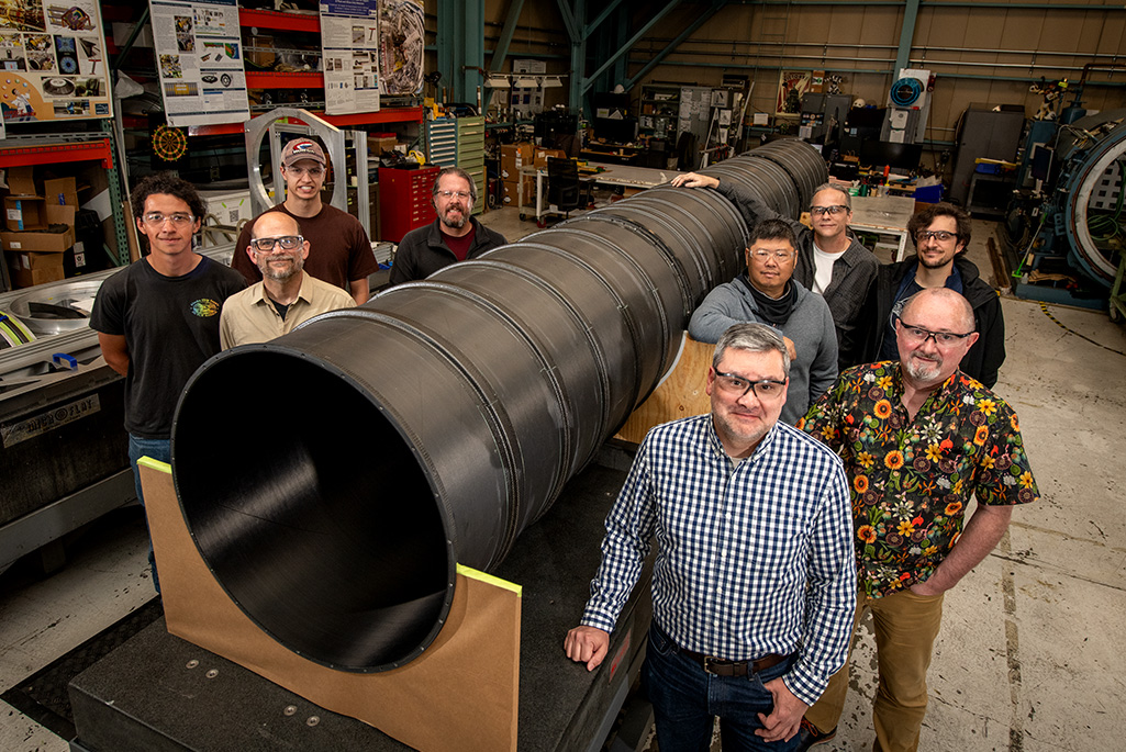 The ATLAS Pixel Support Tube builders and fabricators, photographed next to the Pixel Support Tube, in the Engineering Division's Mechanical Fabrication Shops (April 24, 2026) - Credit: Thor Swift, Berkeley Lab
