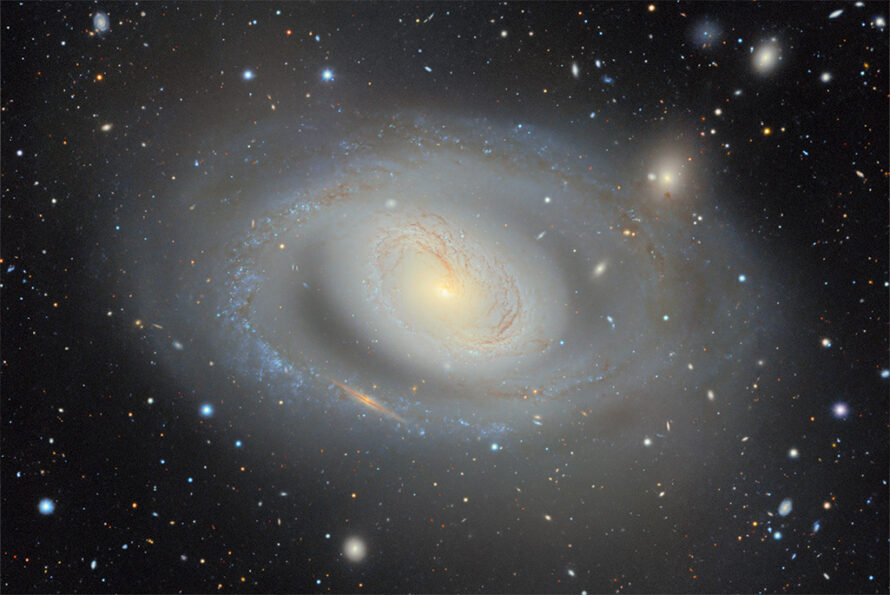 A bright spiral galaxy on a black background dotted with other stars and galaxies.