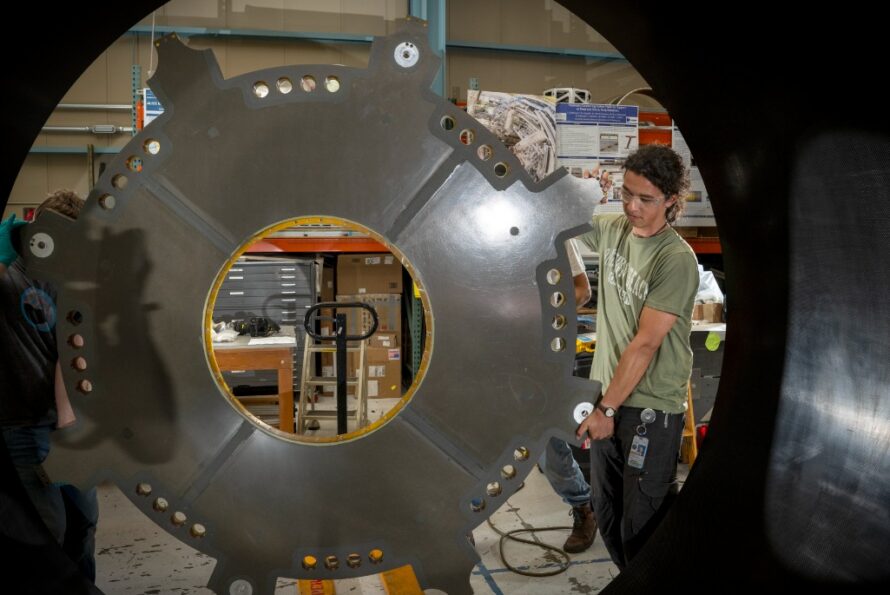 Mechanical Technician Marcos Toledo McGee lifts a component of the ATLAS Detector carbon fiber cylinder into place in the Engineering Division’s shop facility. (Credit: Thor Swift, Berkeley Lab)