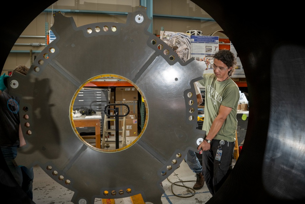 Mechanical Technician Marcos Toledo McGee lifts a component of the ATLAS Detector carbon fiber cylinder into place in the Engineering Division’s shop facility. (Credit: Thor Swift, Berkeley Lab)